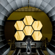 An engineer stands in front of six of the James Webb Space Telescope's mirrors